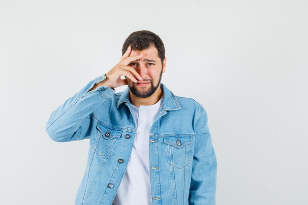 Homem de estilo retro olhando por entre os dedos na jaqueta, camiseta e parecendo chateado. vista frontal.