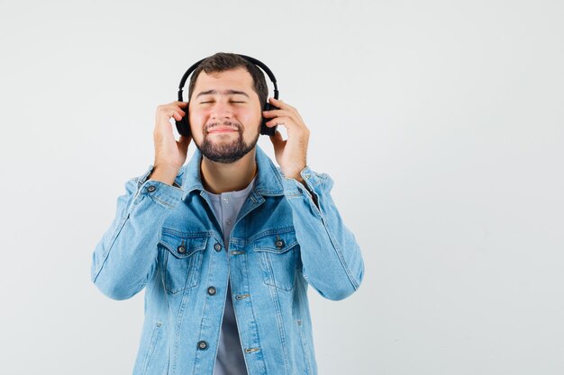 Homem de estilo retro ouvindo música com fones de ouvido na jaqueta, camiseta e parecendo calmo. vista frontal. espaço para texto