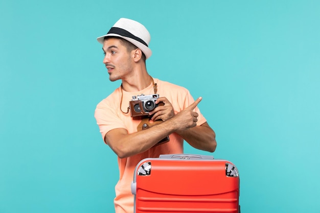 homem de férias com sua grande mala vermelha e câmera tirando fotos em azul