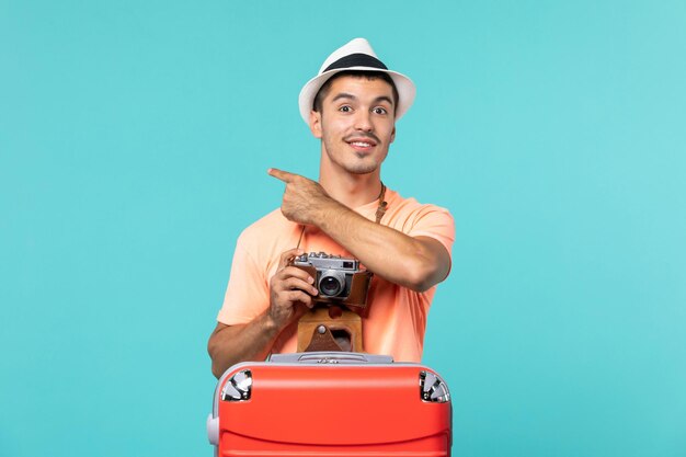 homem de férias com sua grande mala vermelha e câmera tirando fotos em azul