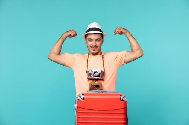 homem de férias com sua mala vermelha e câmera flexionando no azul