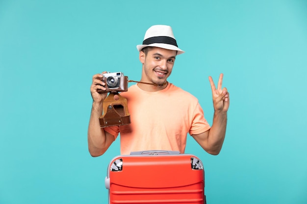 homem de férias com sua mala vermelha tirando fotos com a câmera em azul