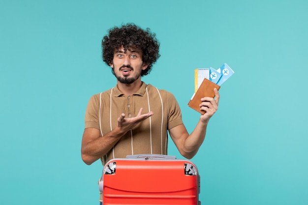 homem de férias segurando ingressos na parede azul