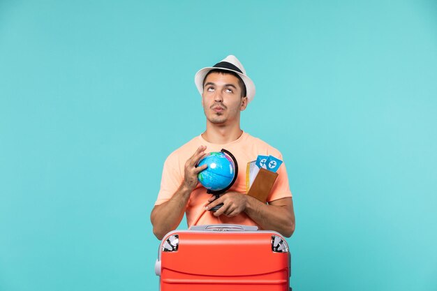 homem de férias segurando um globo com passagens de avião em azul