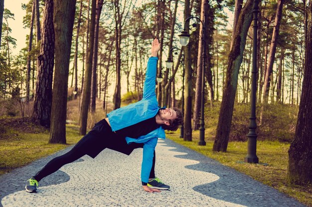 Homem de fitness flexível em uma jaqueta esportiva azul exercitando lá fora.