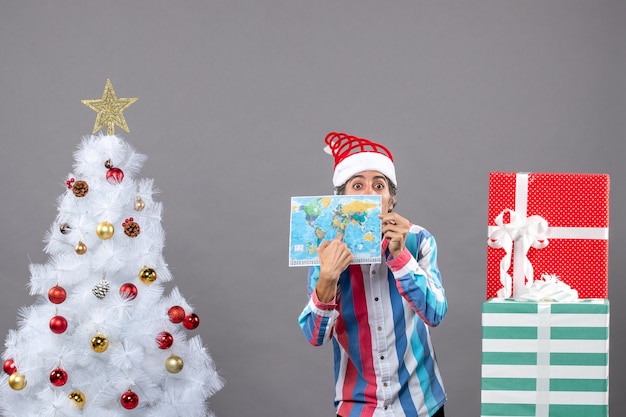 Homem de frente para a surpresa com chapéu de Papai Noel em espiral apontando para o mapa do mundo