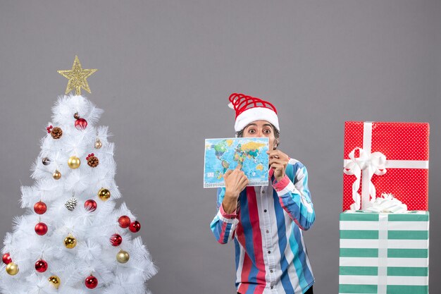 Homem de frente para a surpresa com chapéu de Papai Noel em espiral apontando para o mapa do mundo