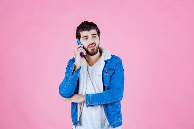 Homem de jaqueta jeans, falando ao telefone celular.