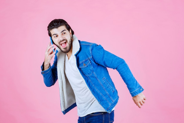 Homem de jaqueta jeans, falando ao telefone celular.