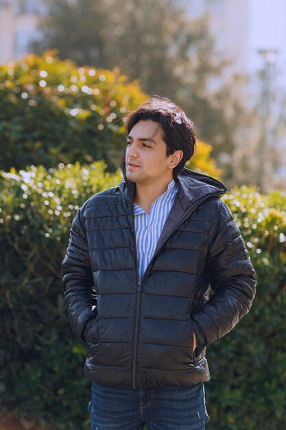 Homem de jaqueta preta em pé no parque e esperando por alguém. Foto de alta qualidade