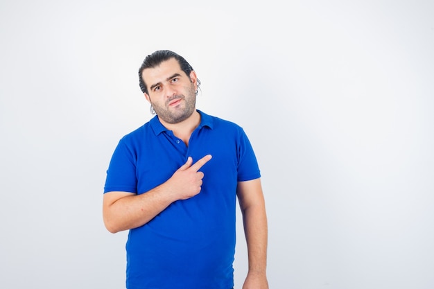 Homem de meia idade apontando para o canto superior direito em uma camiseta azul e parecendo confiante. vista frontal.