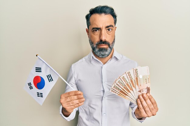 Homem de meia-idade com barba e cabelo cinzento segurando bandeira da coreia do sul e ganhou notas cético e nervoso franzeando a testa chateado por causa do problema pessoa negativa