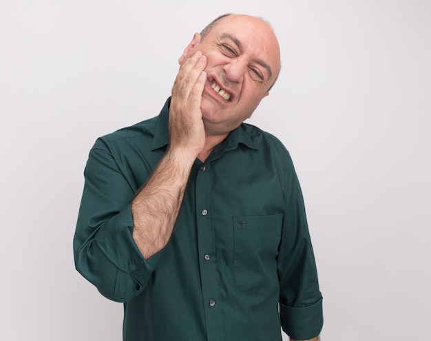 Homem de meia-idade com cabeça inclinada e camiseta verde, colocando a mão na bochecha dolorida, isolada na parede branca com espaço de cópia