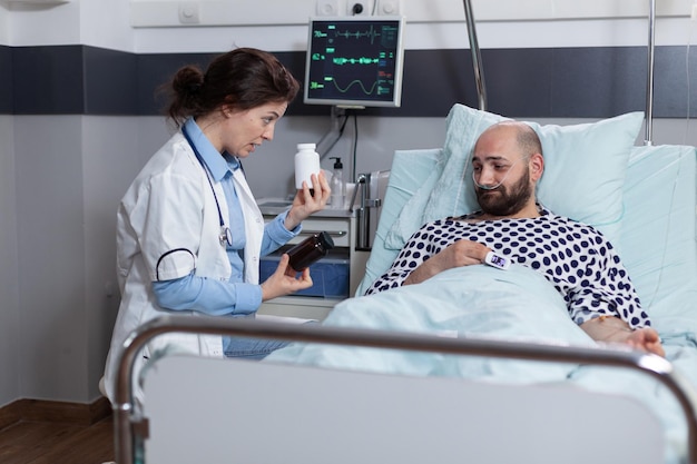 Homem de meia idade com dor após a cirurgia, recebendo escolha de analgésicos prescritos na enfermaria do hospital. médico apresentando frascos de medicamentos para tratamento ao paciente com oxímetro de pulso no dedo.