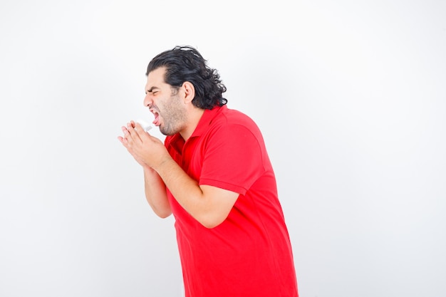 Homem de meia idade em t-shirt vermelha, sofrendo de tosse e parecendo insalubre, vista frontal.