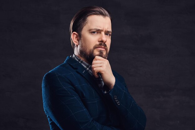 Homem de meia idade pensativo com barba e penteado vestido com um elegante terno azul em um fundo escuro texturizado no estúdio.