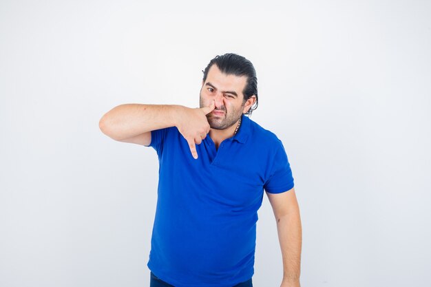 Homem de meia-idade pressionando o polegar no nariz em uma camiseta pólo e olhando para a frente com ar desanimado