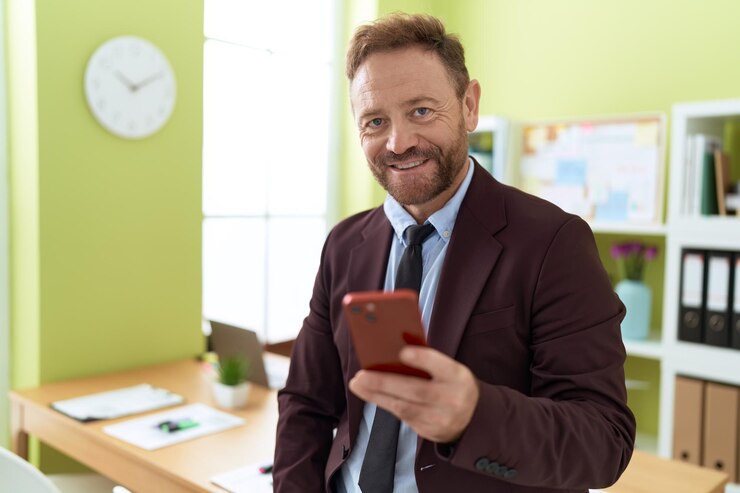 Foto grátis homem de meia-idade trabalhador de negócios sorrindo confiante usando smartphone no escritório