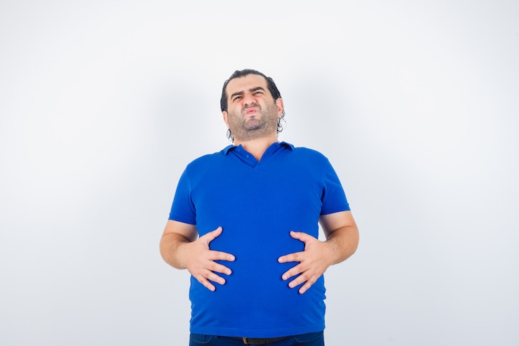 Foto grátis homem de meia idade usando camiseta azul com as mãos na barriga e parecendo indisposto