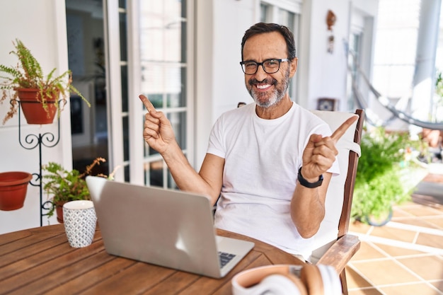 Homem de meia-idade usando computador laptop em casa sorrindo confiante apontando com os dedos para diferentes direções copie o espaço para propaganda