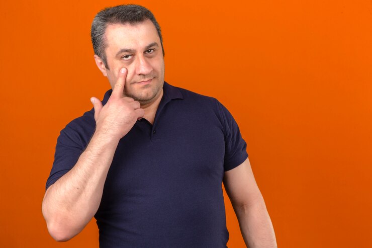 Foto grátis homem de meia idade vestindo camisa polo, apontando para o olho em pé sobre parede laranja isolada