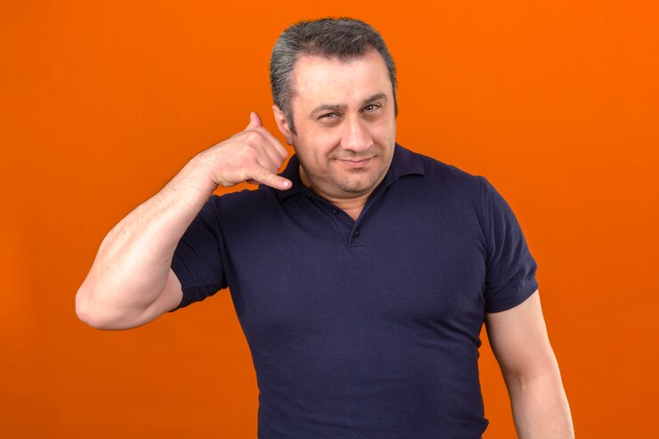 Foto grátis homem de meia idade vestindo camisa polo sorrindo fazendo cal me gesto com os dedos e sorrindo sobre parede laranja isolada