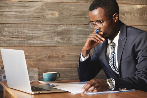 Homem de negócios afro-americano sério olhando para a tela do laptop e pensando