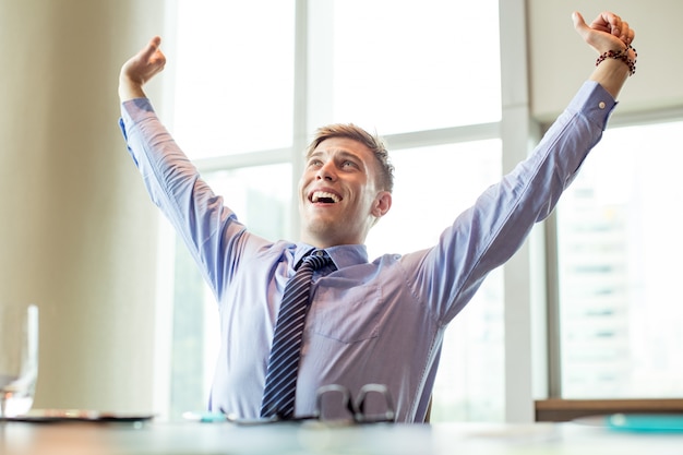 Foto grátis homem de negócios alegre levantando braços na mesa de escritório