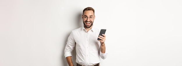 Homem de negócios animado usando telefone celular olhando espantado em pé sobre fundo branco