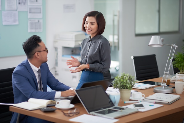 Homem de negócios asiático sentado na mesa de reunião e conversando com colega