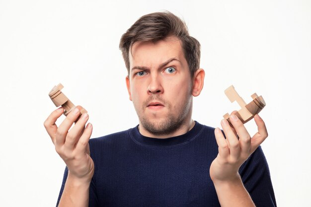Homem de negócios atraente 25 anos olhando confuso com quebra-cabeças de madeira.