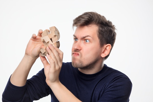 Homem de negócios atraente 25 anos olhando confuso com quebra-cabeças de madeira.