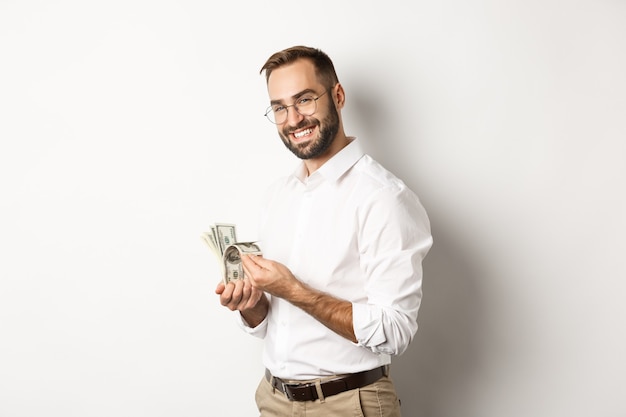 Homem de negócios bem-sucedido contando dinheiro e sorrindo, contra um fundo branco e parecendo satisfeito.