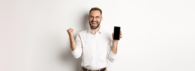 Foto grátis homem de negócios bem sucedido, mostrando a tela do celular, regozijando-se ao ganhar o prêmio on-line, alcançando a meta do aplicativo