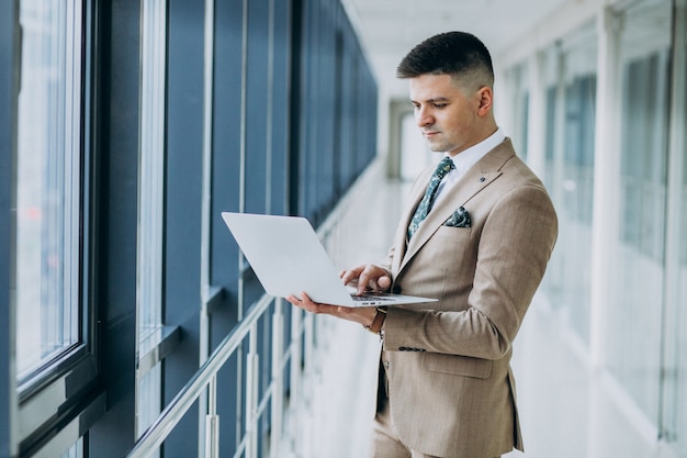 Homem de negócios bonito jovem de pé com o laptop no escritório