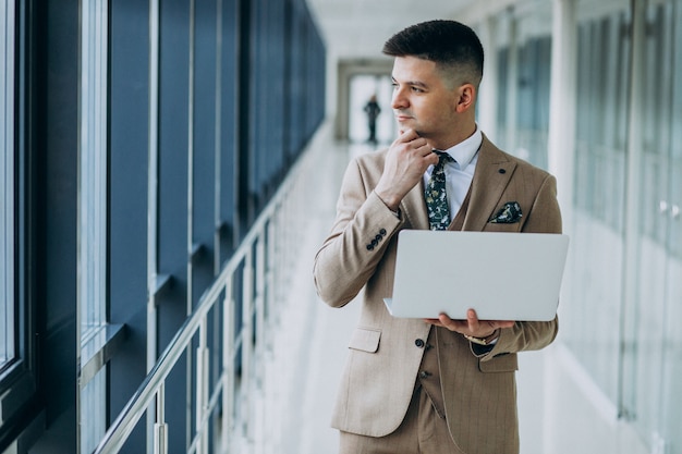 Foto grátis homem de negócios bonito jovem de pé com o laptop no escritório