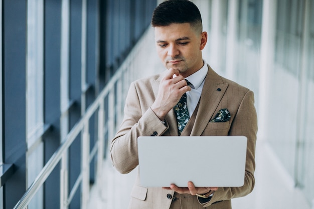 Homem de negócios bonito jovem de pé com o laptop no escritório