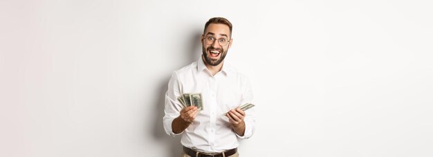 Homem de negócios bonito olhando animado enquanto contava dinheiro em pé sobre fundo branco