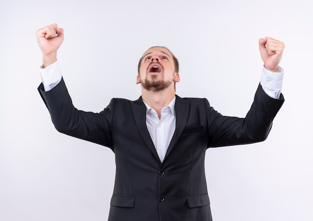 Homem de negócios bonito usando terno cerrando os punhos, feliz e louco, em pé sobre um fundo branco