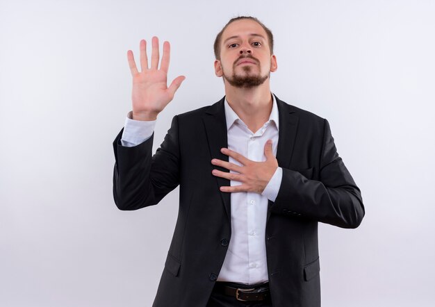 Homem de negócios bonito usando terno fazendo um juramento e parecendo confiante em pé sobre um fundo branco