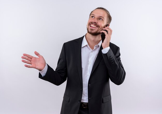 Homem de negócios bonito vestindo terno falando no celular e sorrindo em pé sobre um fundo branco