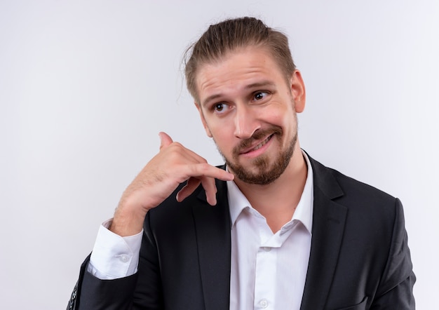 Homem de negócios bonito vestindo terno olhando para o lado fazendo gesto de me chamar de pé sobre um fundo branco