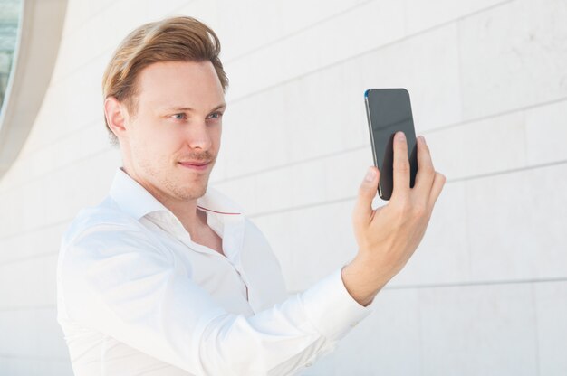 Homem de negócios confiante posando e tirando foto de selfie ao ar livre