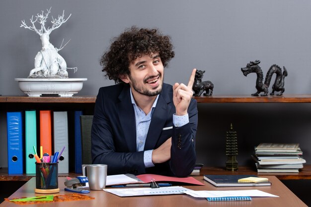 Homem de negócios de cabelo encaracolado de vista frontal surpreendendo com uma ideia sentado na mesa de um escritório moderno