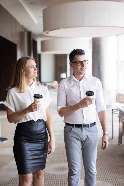 Homem de negócios e mulher de negócios novos de sorriso que andam com café no escritório.
