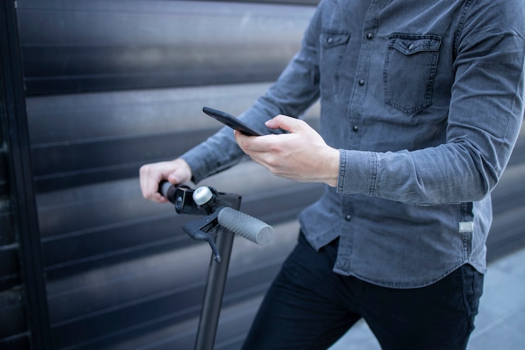 Foto grátis homem de negócios irreconhecível usando o aplicativo em seu smartphone enquanto está de pé em uma scooter elétrica