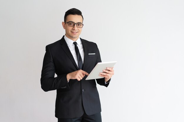 Homem de negócios novo alegre que verifica o email na tabuleta e que olha a câmera.