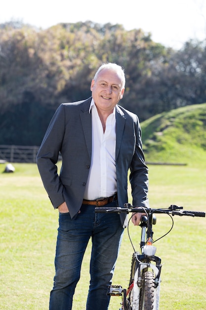 Homem de negócios sênior elegante ao lado de sua bicicleta