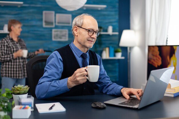 Homem de negócios sênior segurando uma xícara de café e trabalhando em um laptop