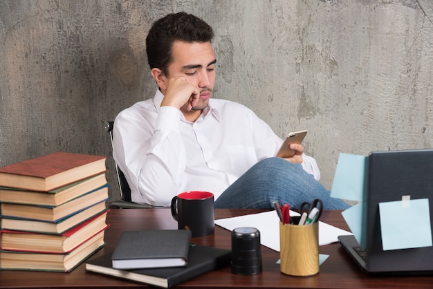 Homem de negócios sério brincando com o telefone na mesa do escritório.